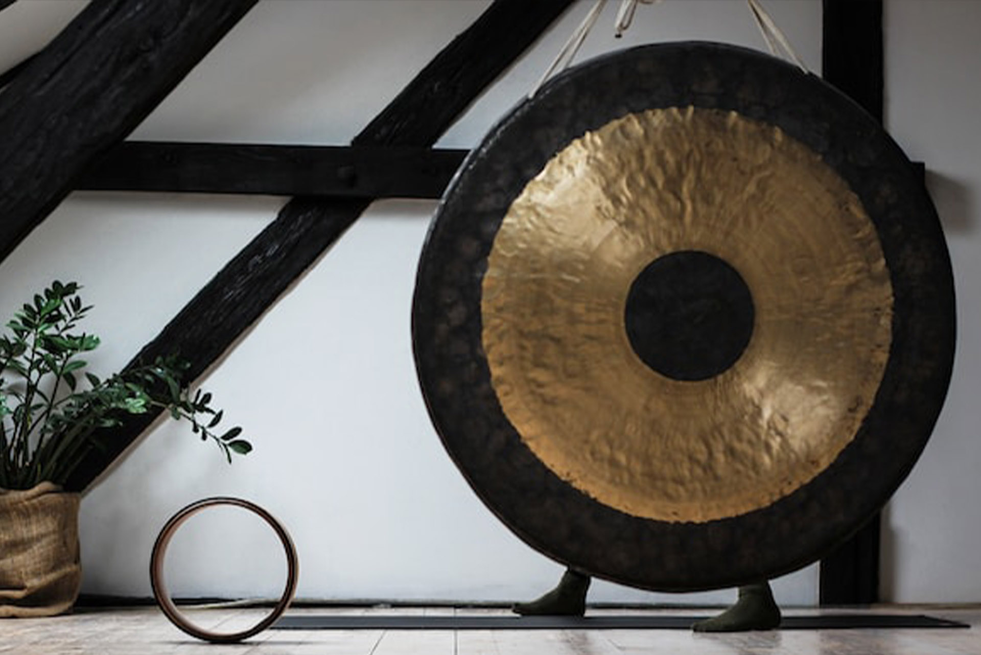 Un Gong dorado y negro al lado de una planta y un círculo en un desván blanco con vigas de madera